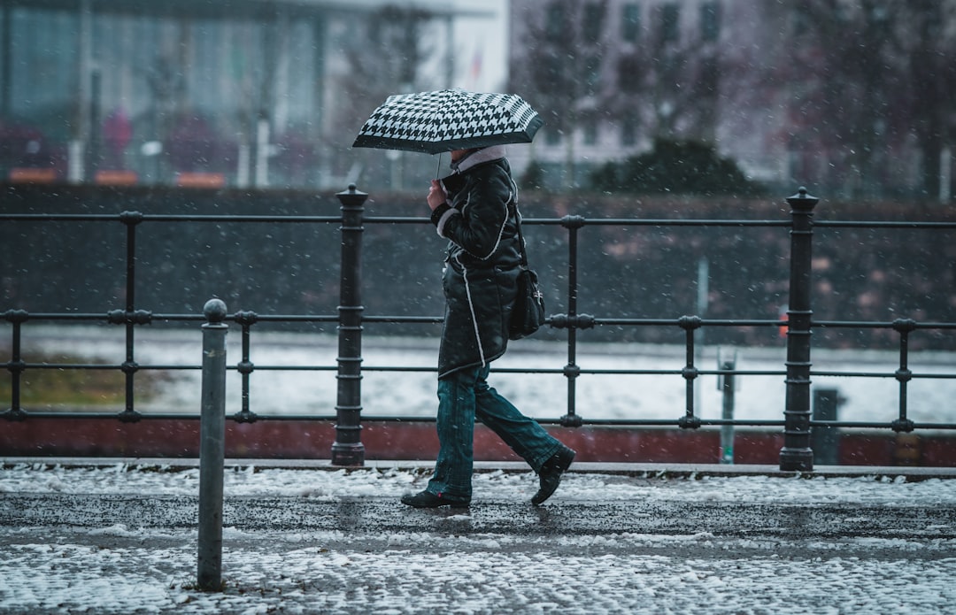 person in black jacket and blue denim jeans holding umbrella walking on snow covered road during