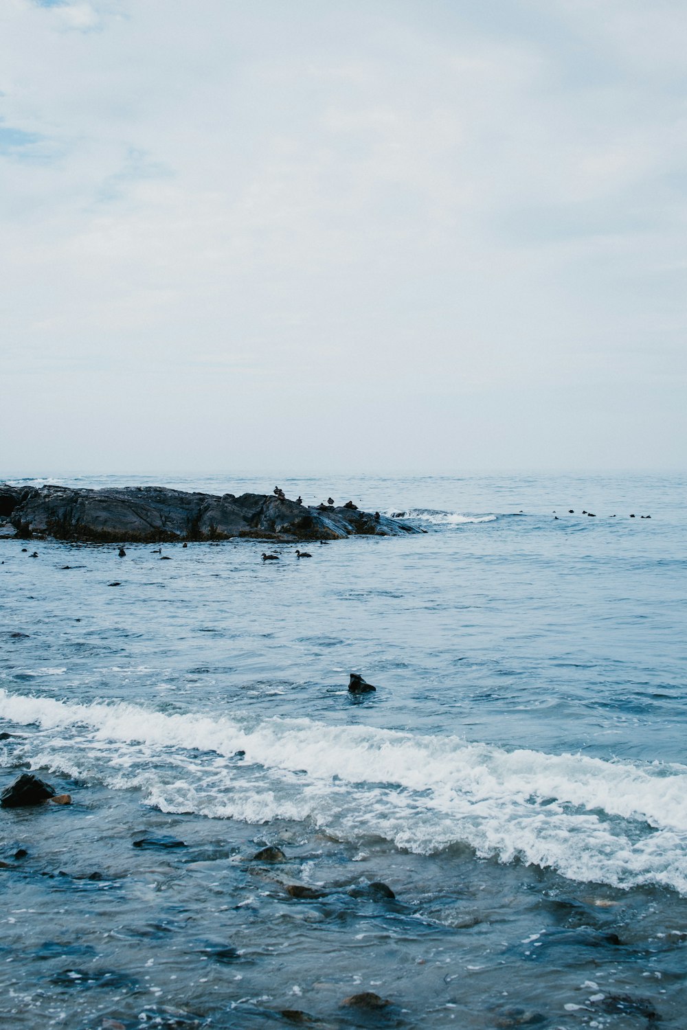 ocean waves crashing on rocks under white cloudy sky during daytime