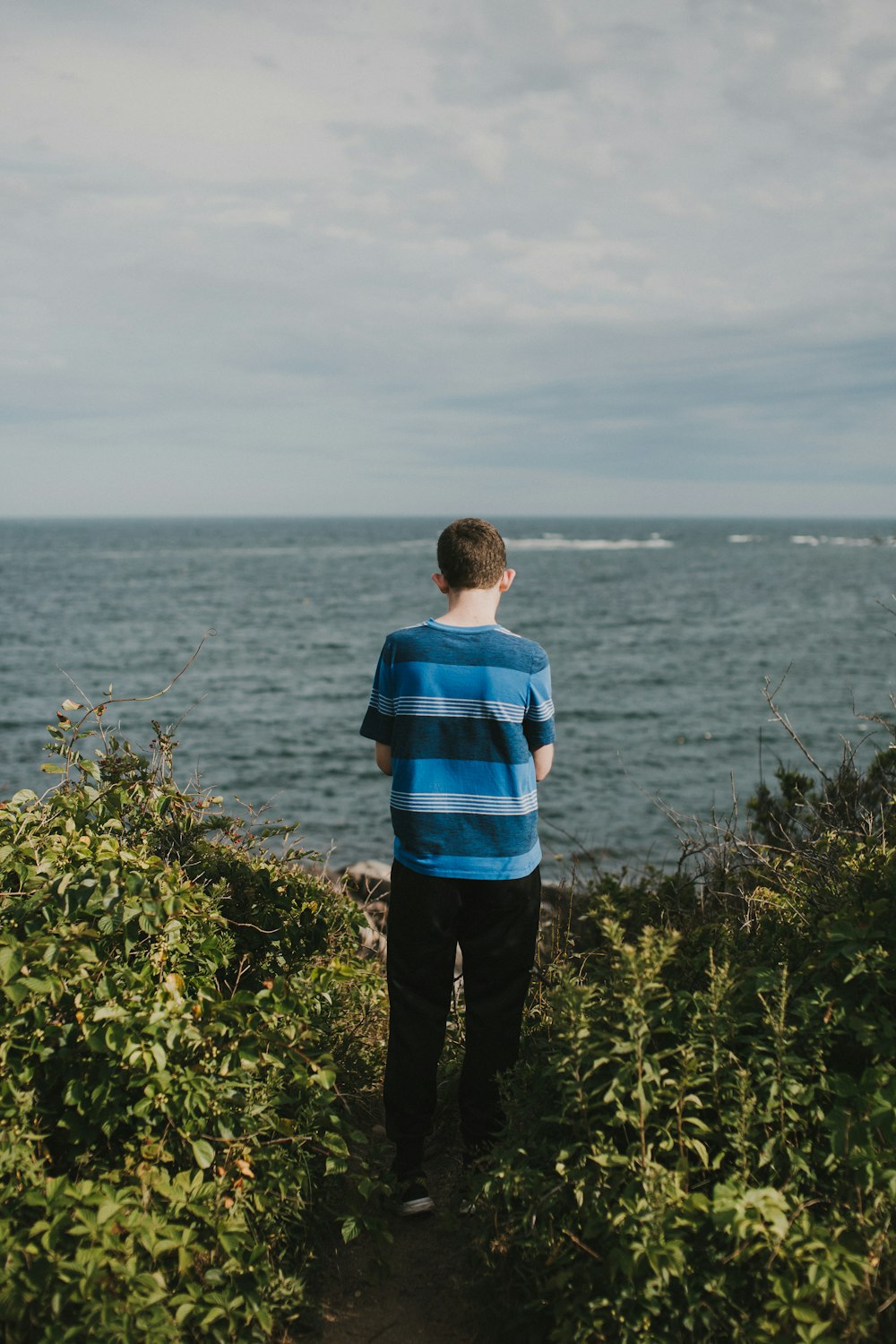 man in blue and black striped shirt standing on green grass field near body of water