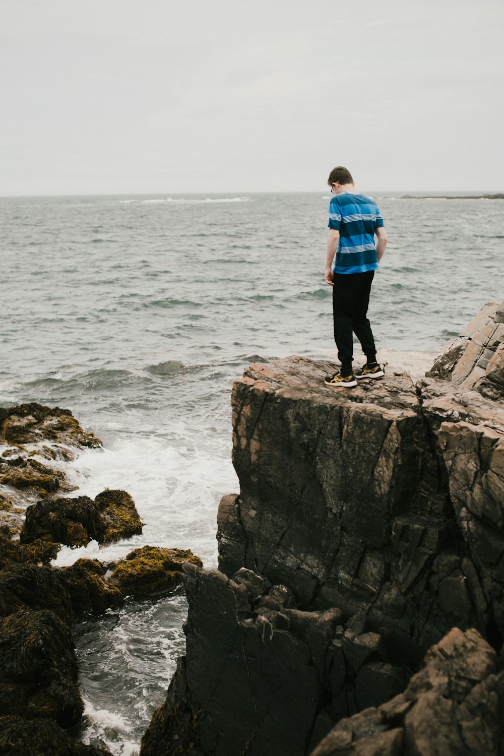 man in blue and black plaid dress shirt standing on rock formation near sea during daytime