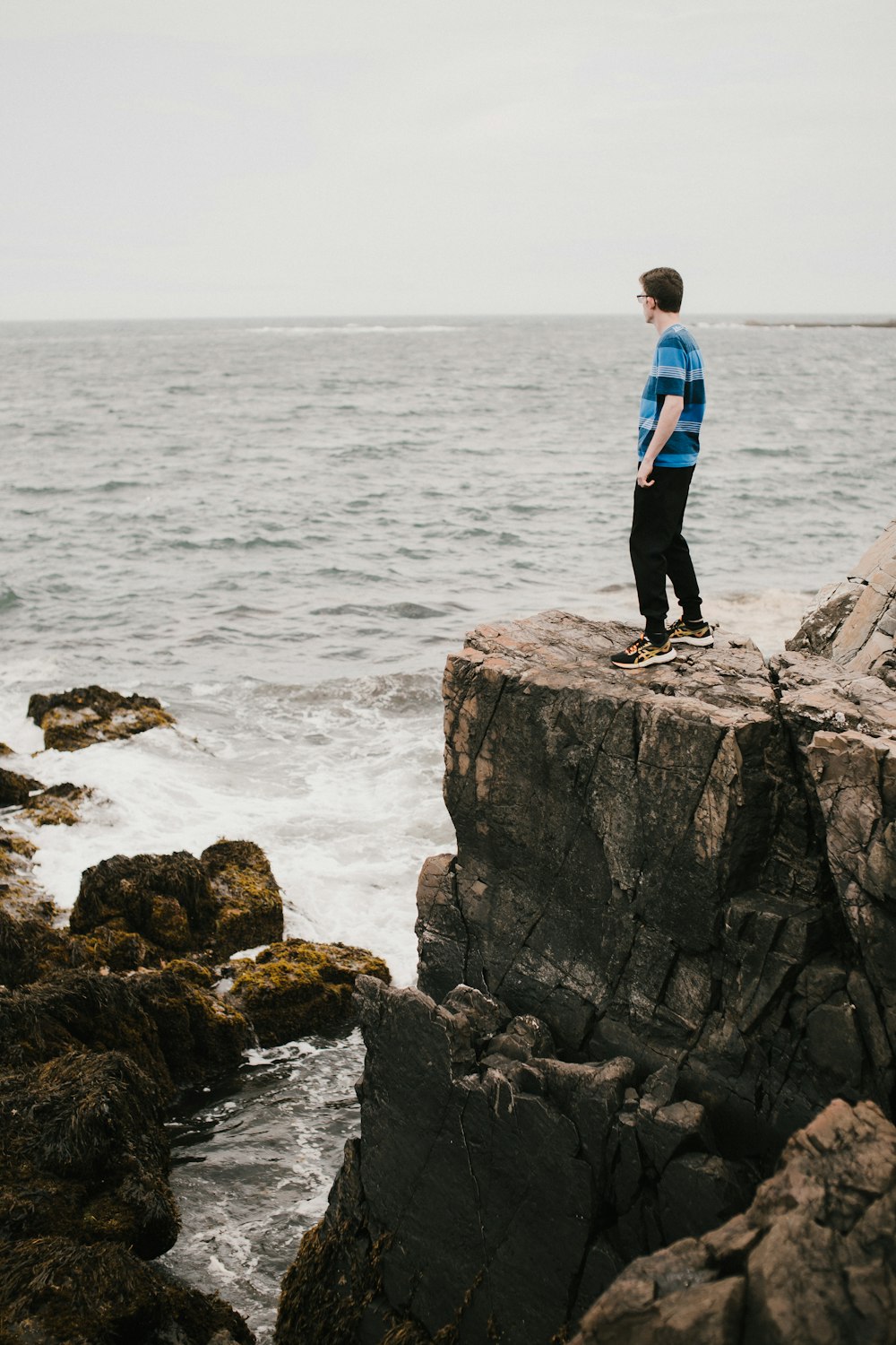 man in blue jacket standing on rock formation near body of water during daytime