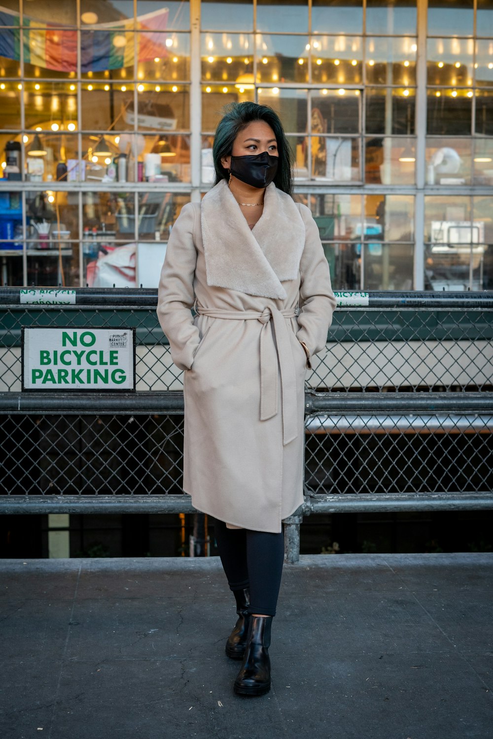 woman in beige coat standing beside black metal fence