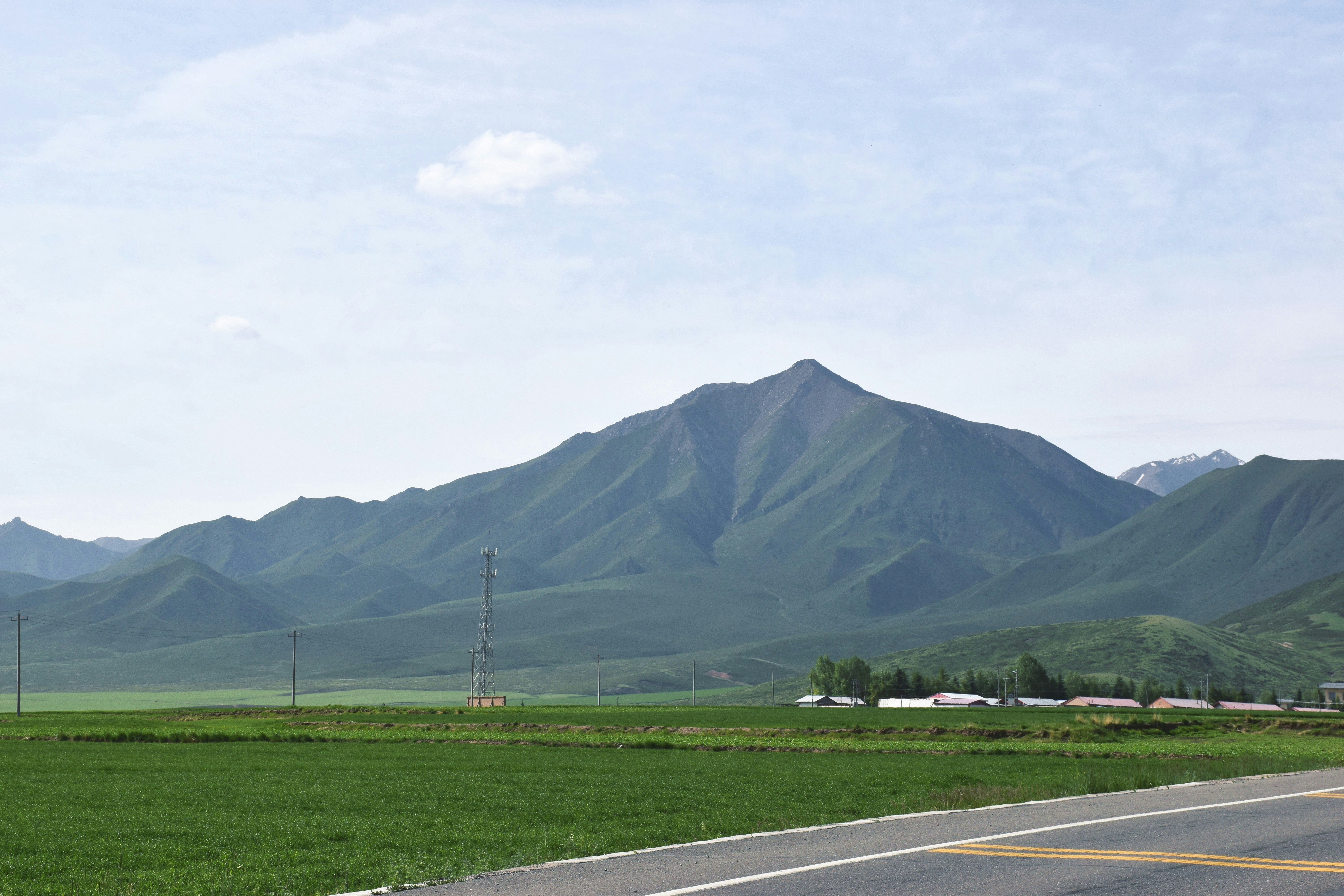 green grass field near mountain under white sky during daytime