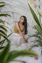 Woman enjoying a peaceful self-massage session in a cozy, sunlit room filled with plants.