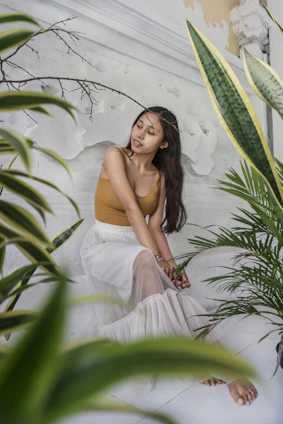 A serene woman sitting peacefully in a sunlit room surrounded by soft pastel colors and plants.