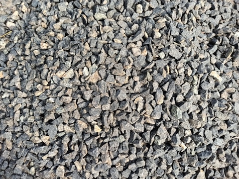 A densely packed pile of small, irregularly shaped gray and brown stones with various textures and shades. The stones appear rough and are closely arranged, suggesting they might be used for construction or landscaping purposes.