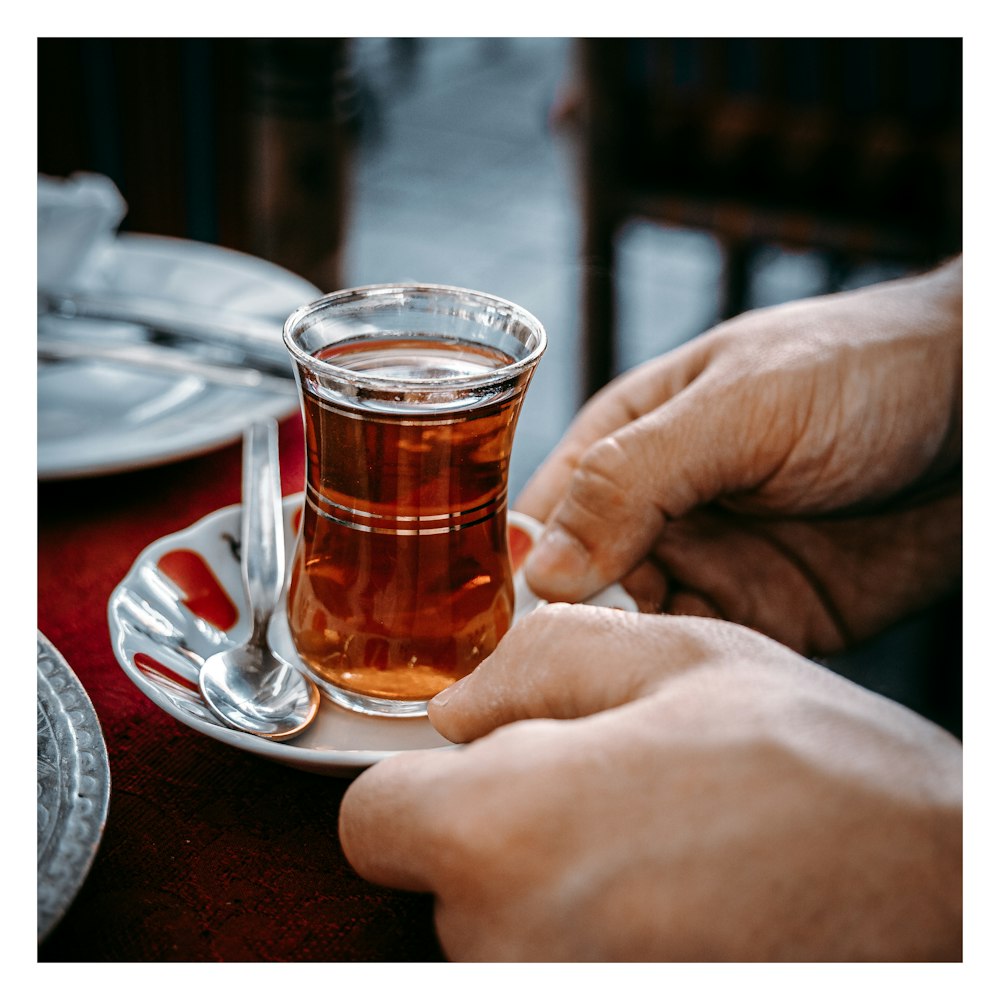 person holding clear glass mug with brown liquid