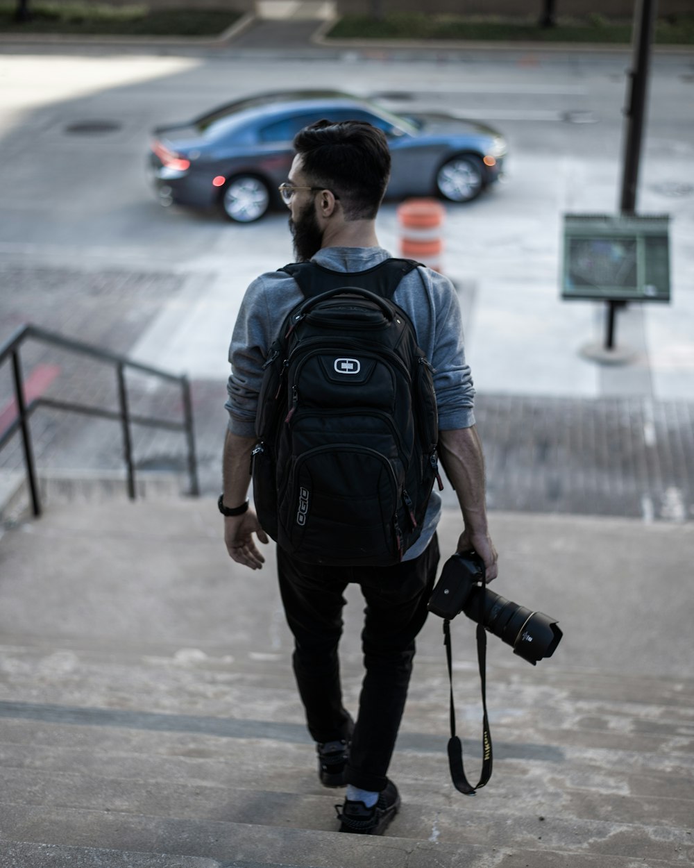 man in blue crew neck t-shirt with black backpack walking on sidewalk during daytime