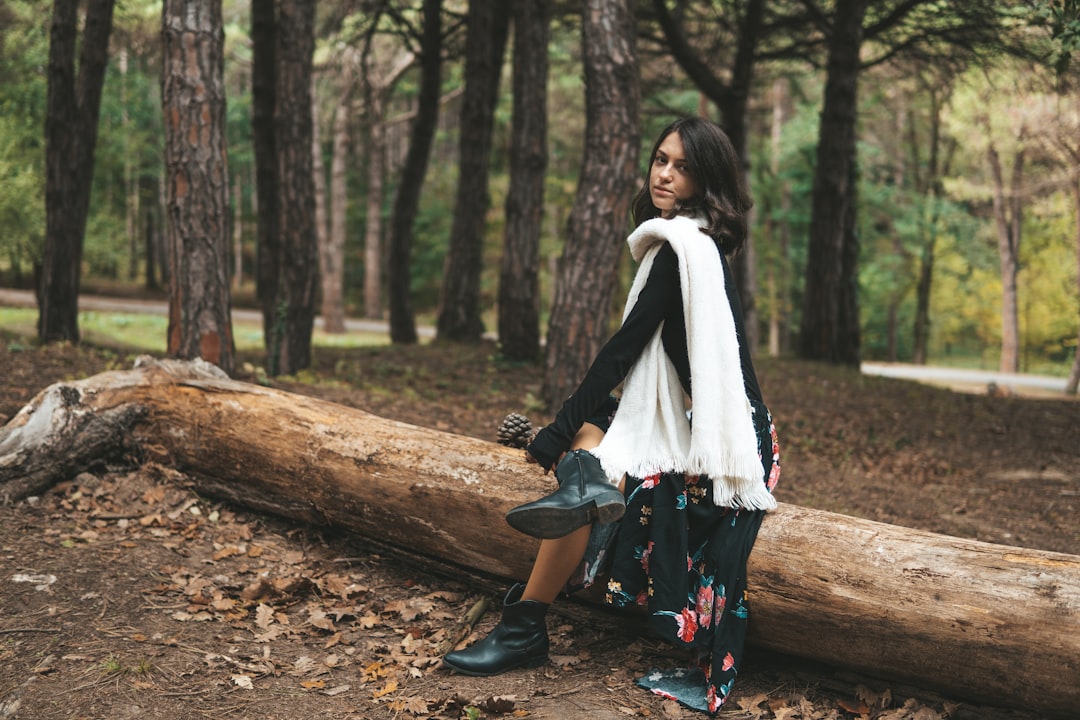 woman in white scarf and black jacket standing on brown tree log during daytime