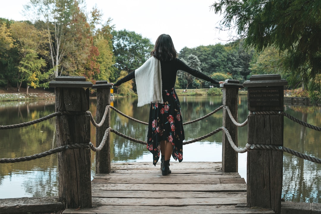 woman in white long sleeve shirt and red skirt standing on wooden bridge during daytime