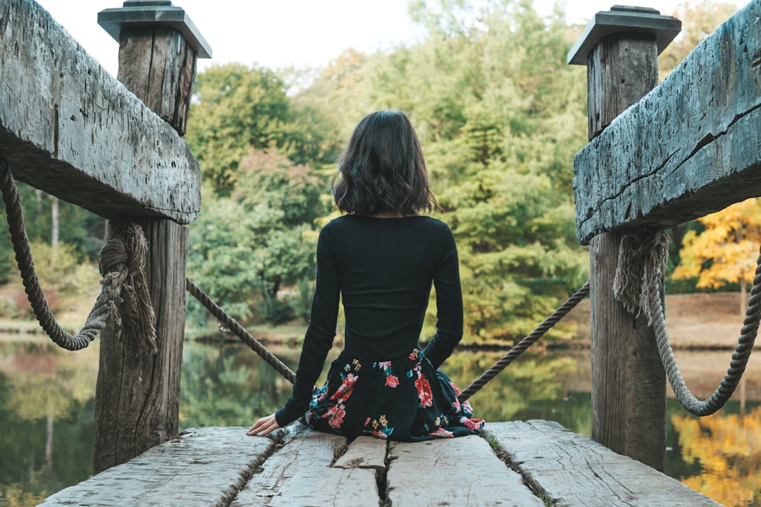 woman in black long sleeve shirt and black and red skirt sitting on brown wooden bridge