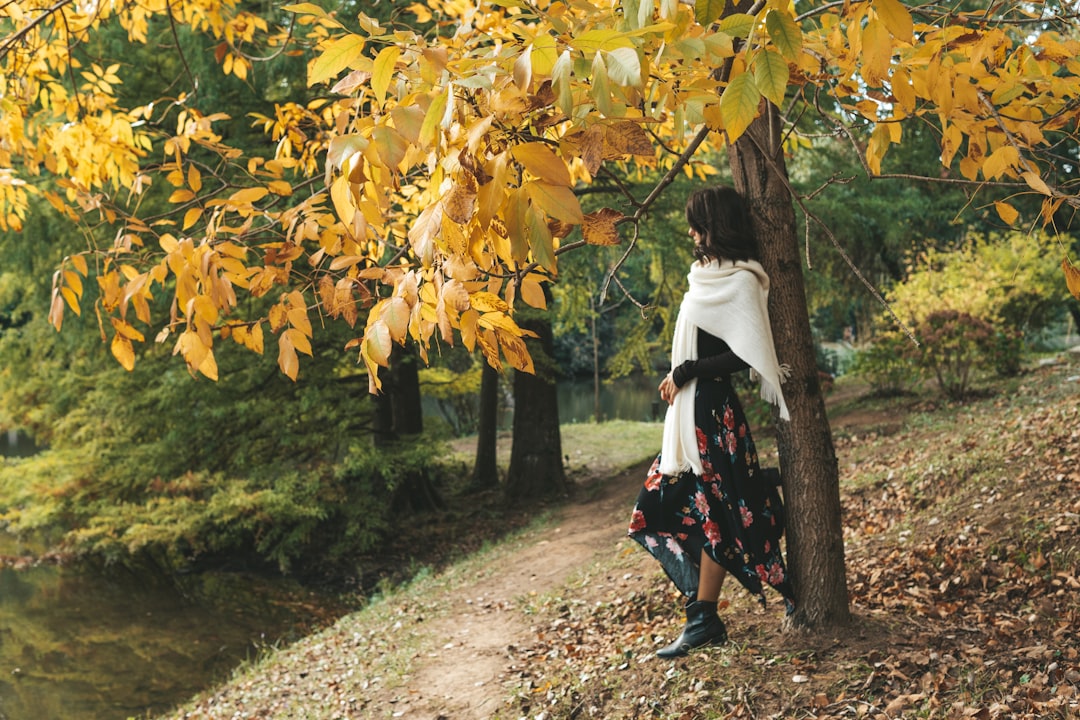 woman in white long sleeve shirt and red skirt walking on pathway between yellow leaves trees