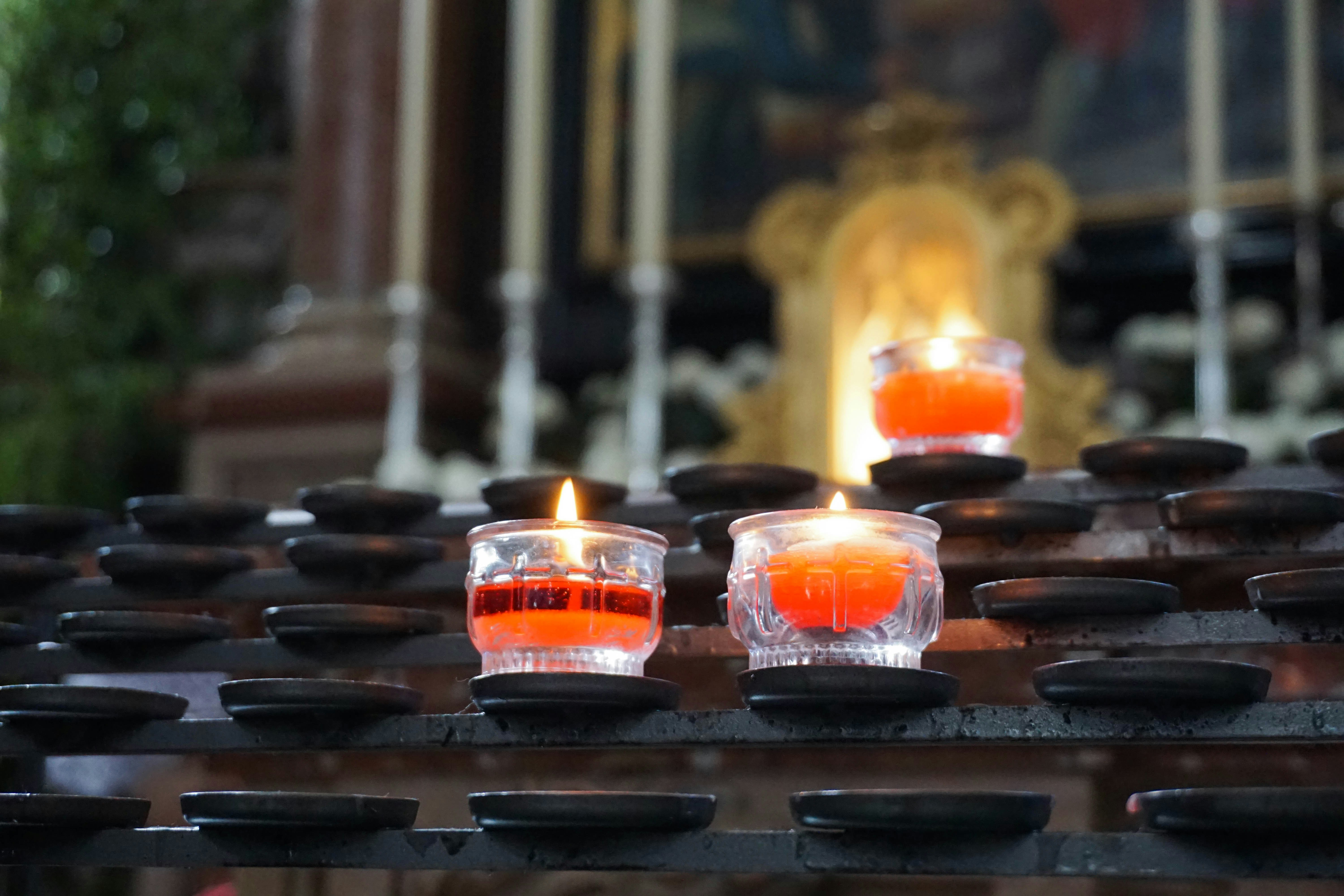 Lit prayer candles glow in a metal holder at a church.
