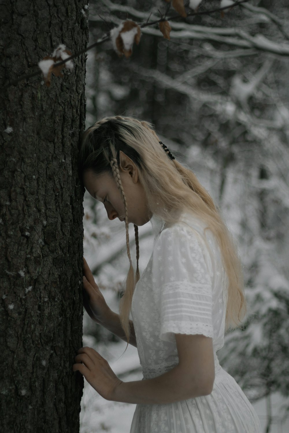 Mujer en vestido blanco apoyada en el árbol