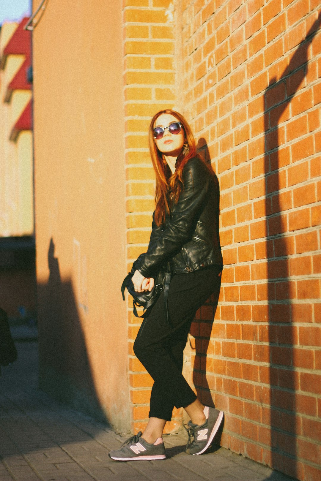 woman in black leather jacket and black pants leaning on brown wall