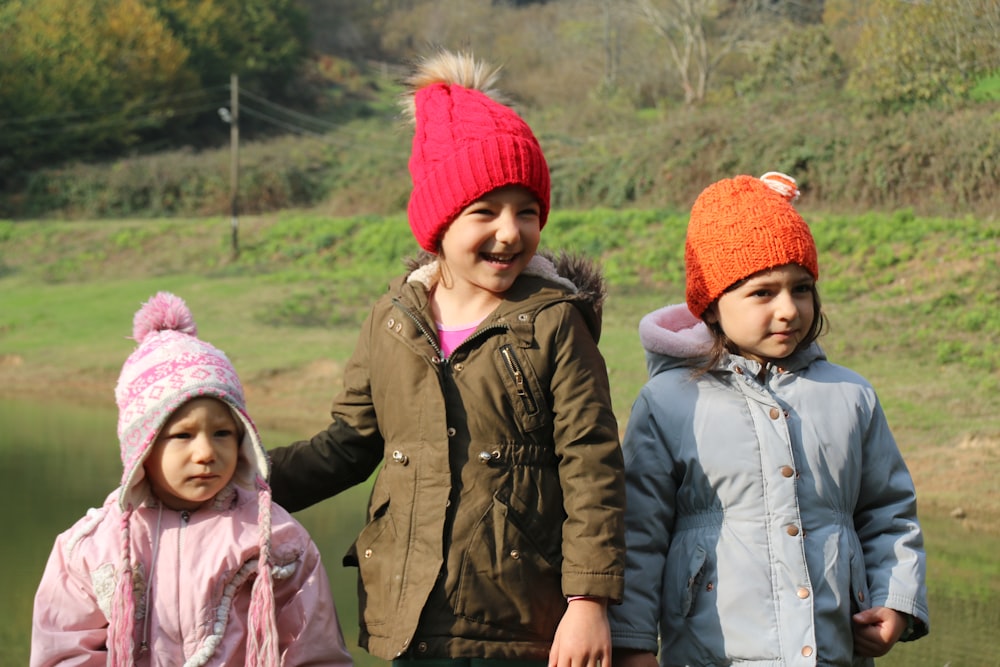 girl in red knit cap and brown jacket standing beside girl in red knit cap
