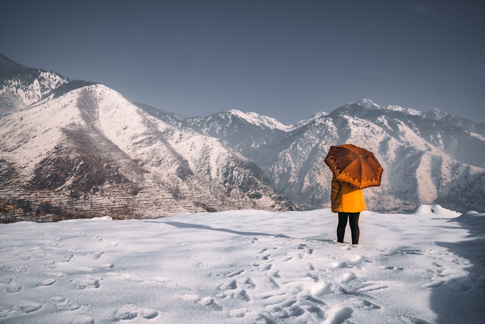 Persona con chaqueta naranja de pie en el suelo cubierto de nieve durante el día