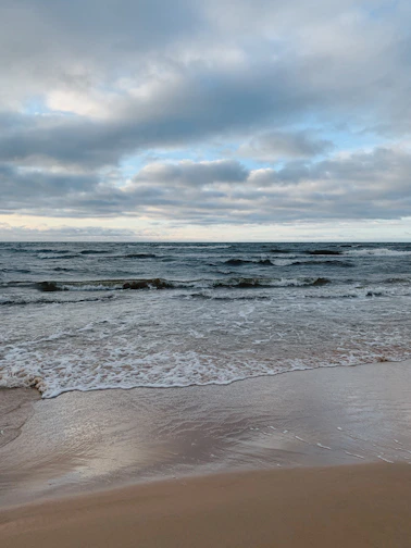 ocean waves crashing on shore under cloudy sky during daytime