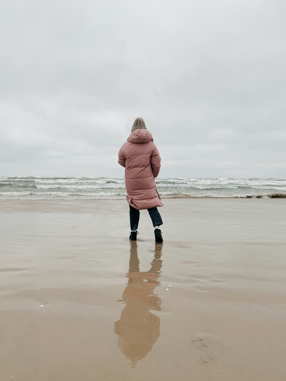 woman in pink hoodie standing on beach during daytime