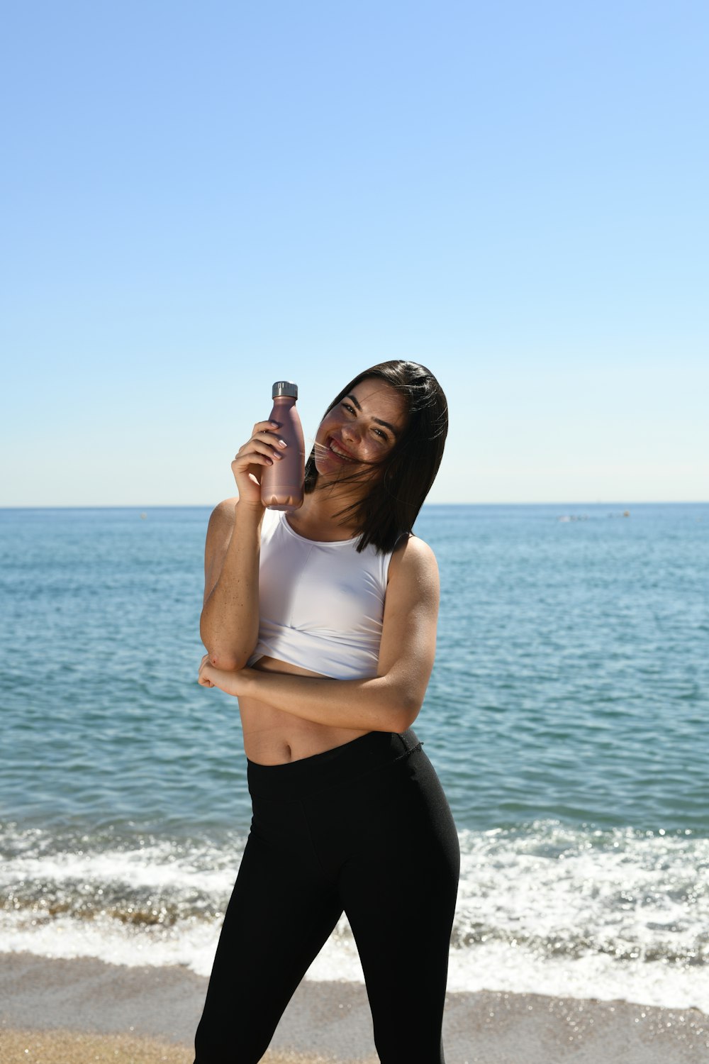 woman in white tank top and black pants standing on beach during daytime
