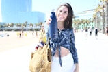 A smiling woman wearing a macramé bracelet holding a cotton canvas tote on a sunny beach