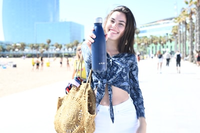 A smiling woman wearing a macramé bracelet holding a cotton canvas tote on a sunny beach