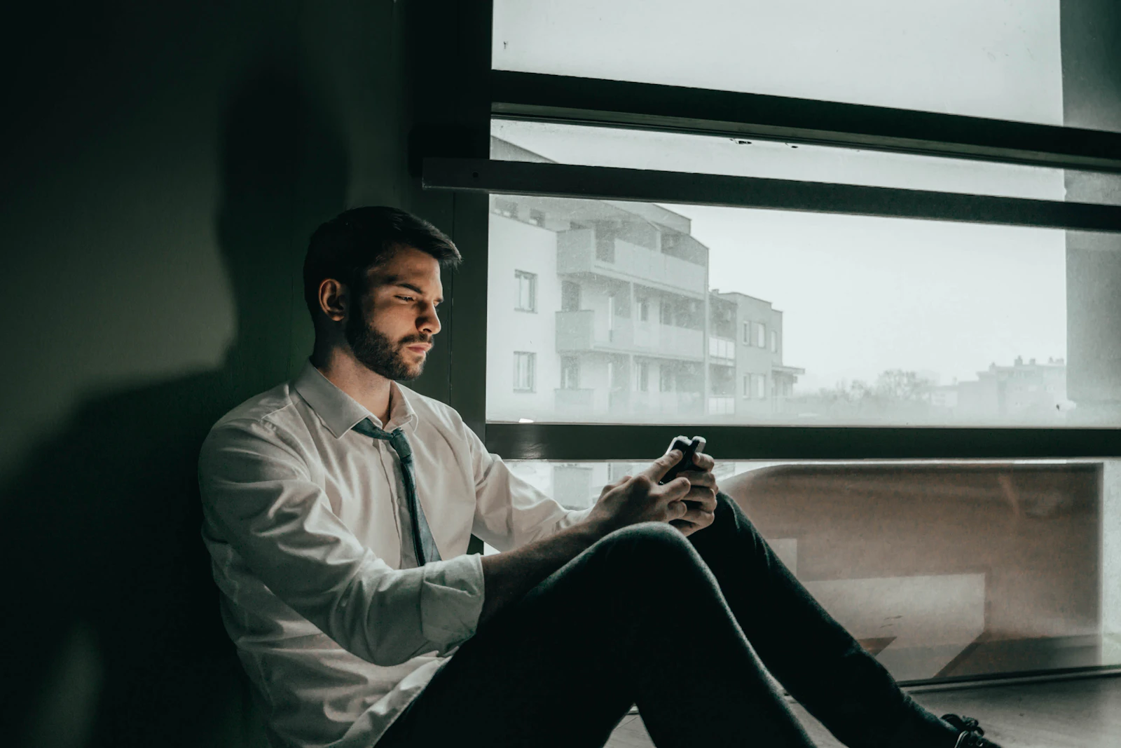 Homem sentado junto a uma janela com luz suave, lendo uma mensagem no celular em ambiente calmo e profissional