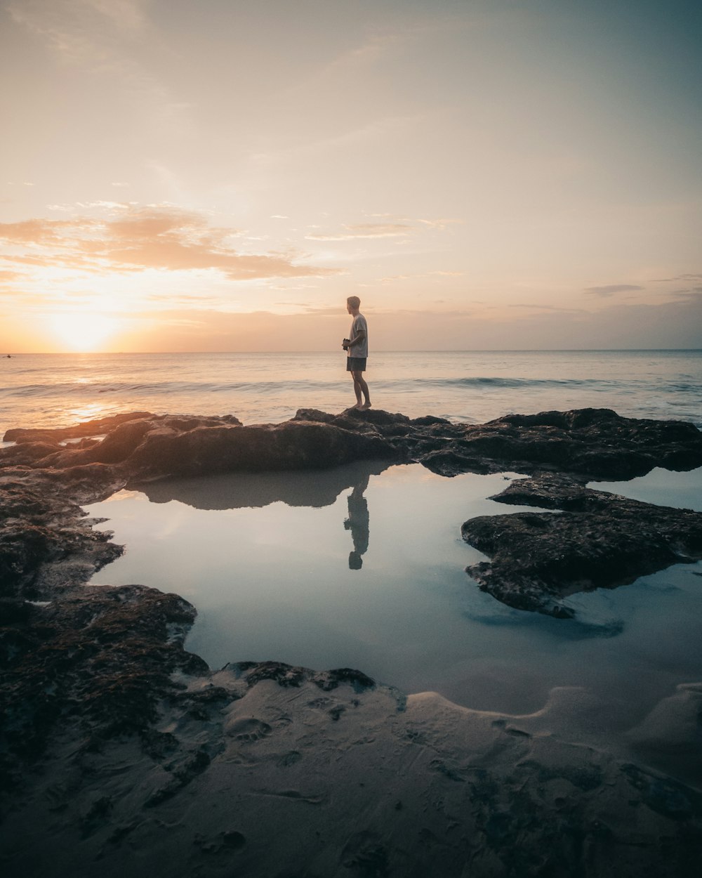man standing on rock formation in the middle of sea during sunset