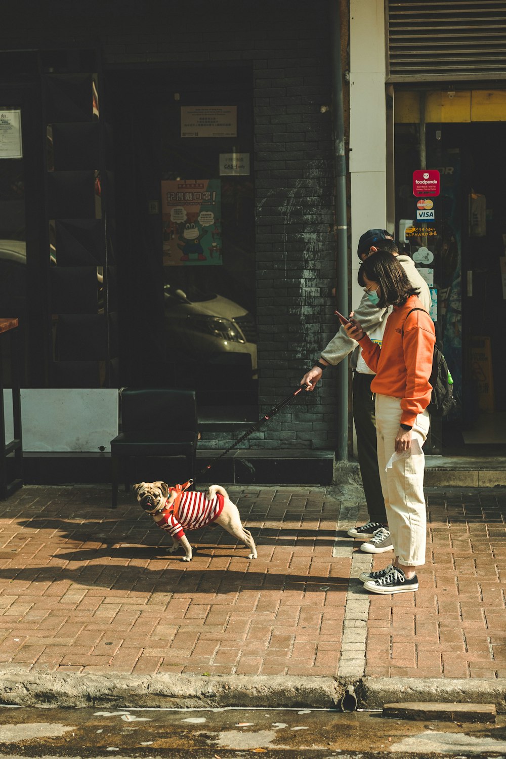 Hombre con chaqueta naranja y pantalones blancos sosteniendo correa de perro negro