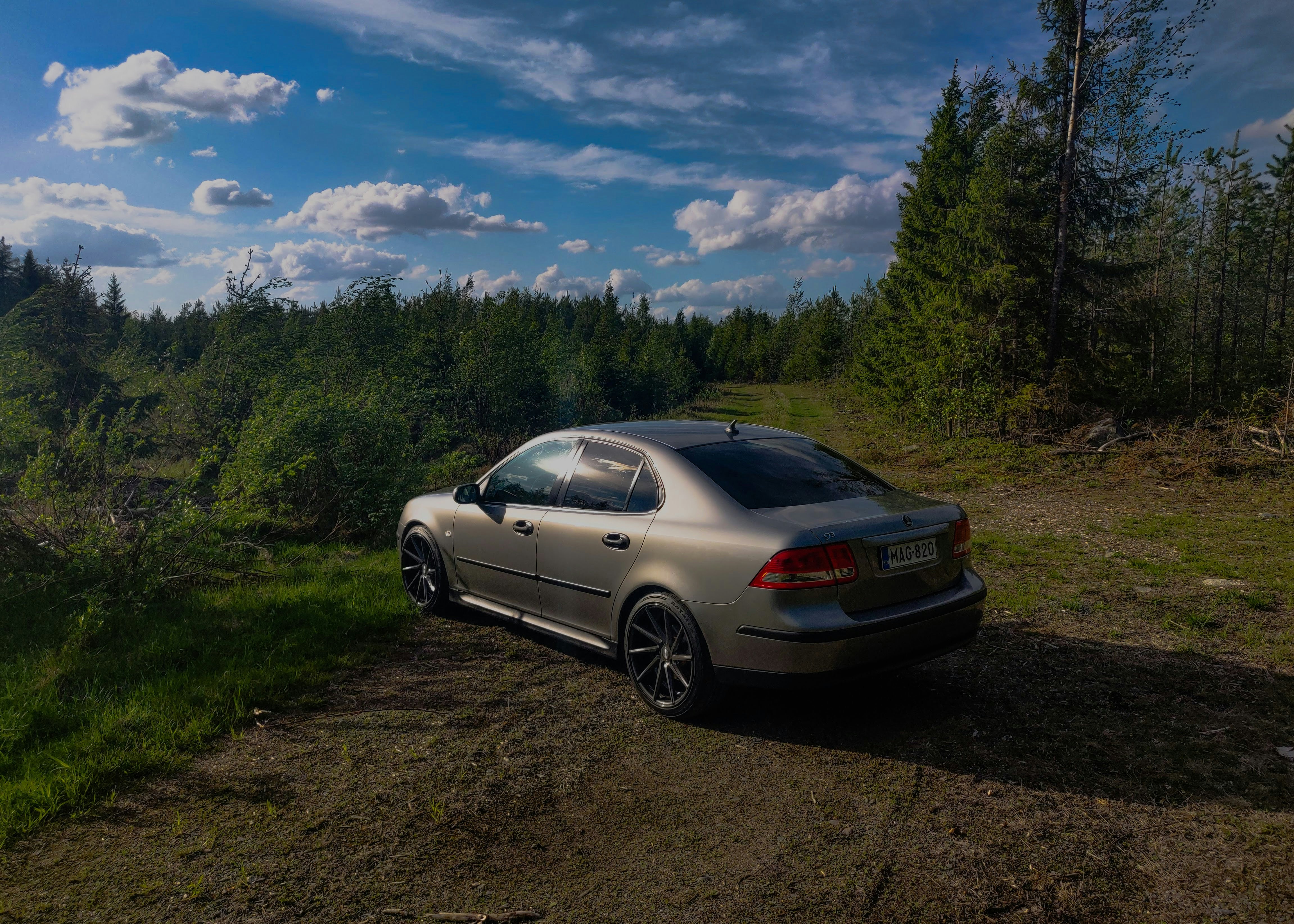silver bmw coupe parked on dirt road near green trees under blue sky and white clouds