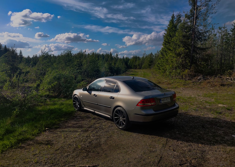 silver bmw coupe parked on dirt road near green trees under blue sky and white clouds