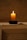 A minimalist candle on a dark wooden table with a blurred background.