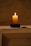 A softly lit candle glowing on a wooden table with a beige linen backdrop.
