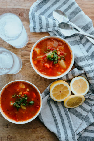 A rustic wooden table with a steaming bowl of homemade vegetable soup garnished with fresh herbs.