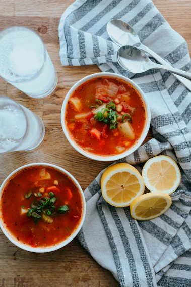 A colorful bowl of fresh vegetable soup steaming on a rustic wooden table.