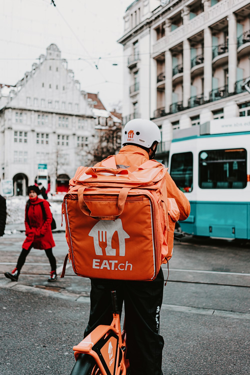 Mann in orangefarbener Jacke und schwarzer Hose mit weißem Helm tagsüber auf dem Bürgersteig