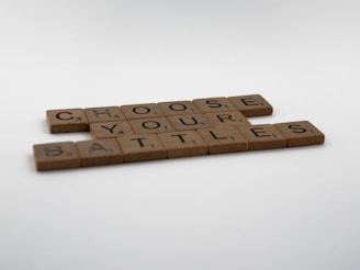 Wooden letter tiles arranged to form the phrase 'CHOOSE YOUR BATTLES' against a plain white background.