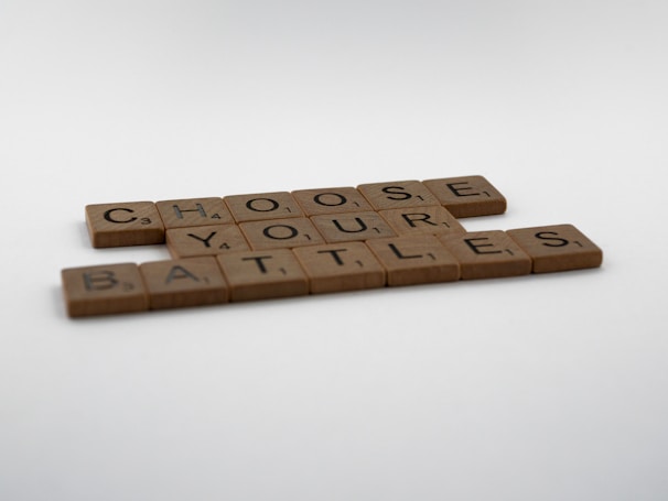 Wooden letter tiles arranged to form the phrase 'CHOOSE YOUR BATTLES' against a plain white background.