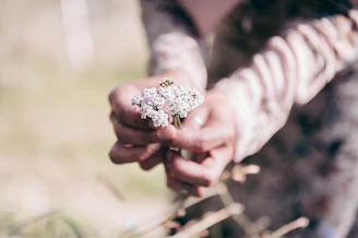 A soft-focus photo of a woman holding a delicate bouquet of wildflowers in a sunlit garden.