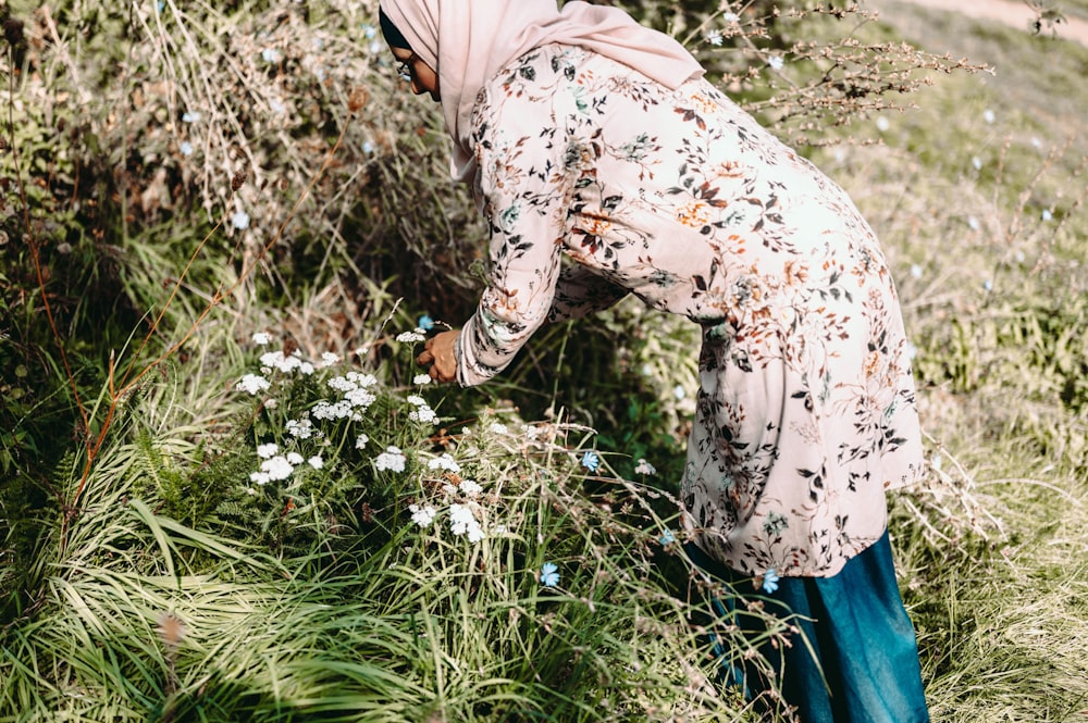 woman in beige and brown floral long sleeve shirt and blue denim jeans standing on green