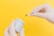 A pair of gloved hands holding a small white container and a swab with a brown substance against a bright yellow background.