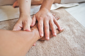 Hands gently massaging a person's ankle, surrounded by soft beige towels, creating a calming and relaxing atmosphere.