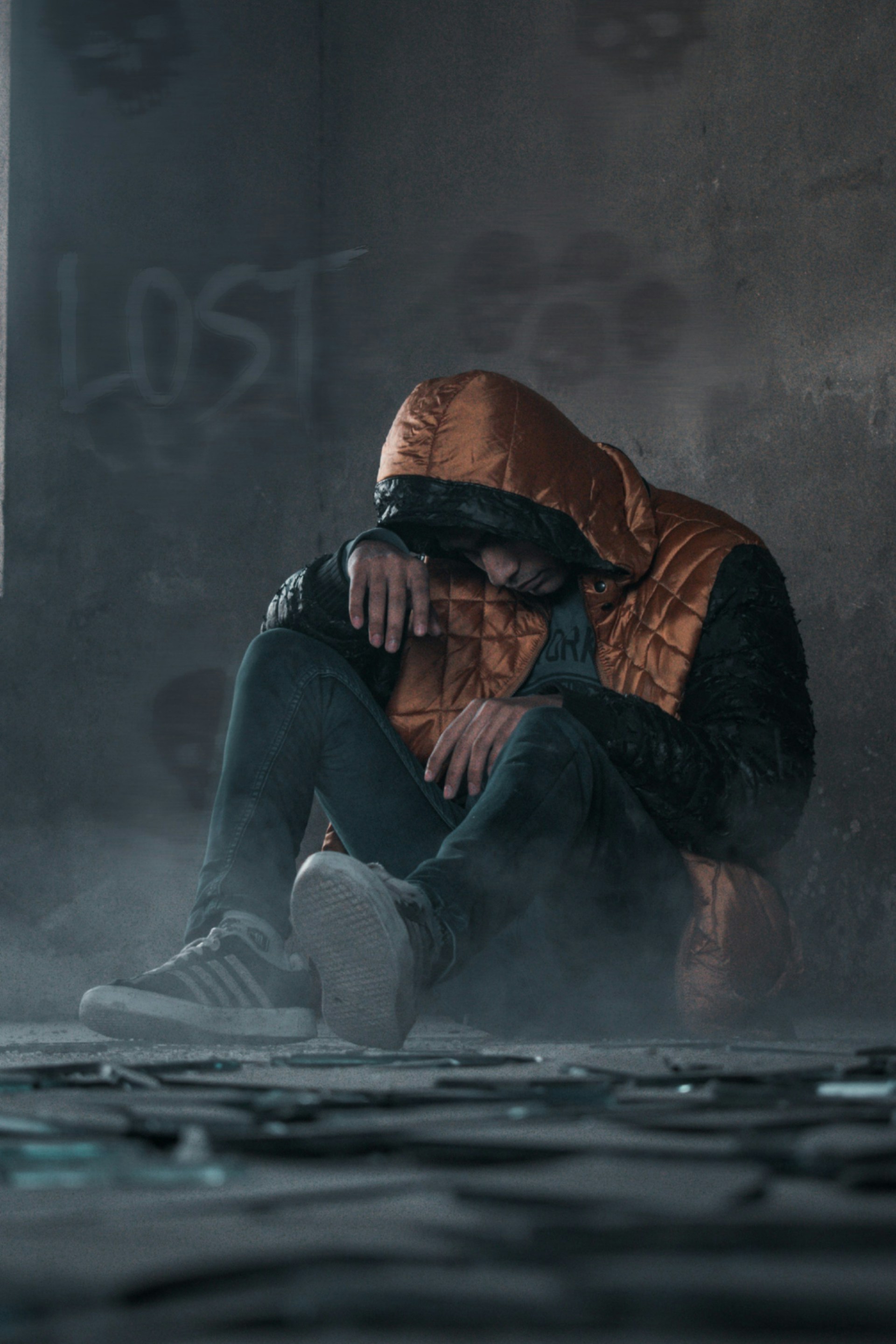 man in orange hoodie and gray pants sitting on floor