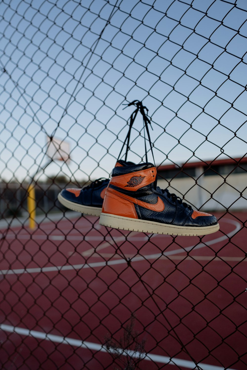 orange and black nike athletic shoes on chain link fence