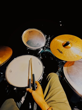 Smiling student holding drumsticks, sitting beside a drum kit with warm lighting.