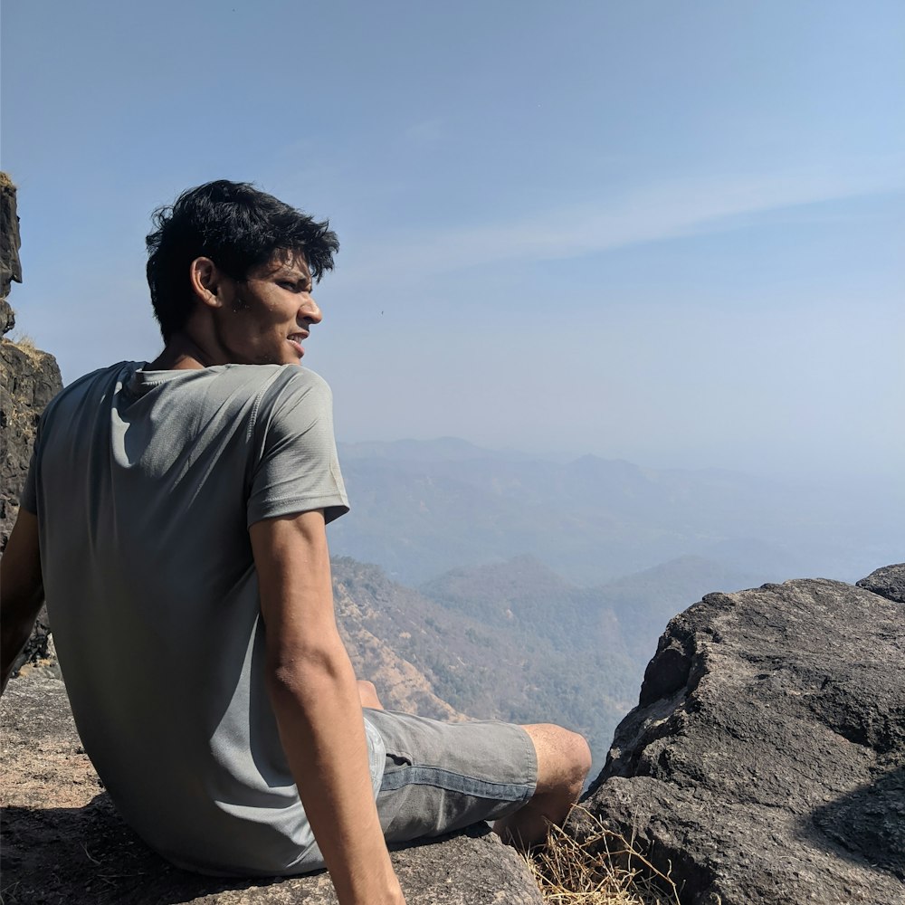 Hombre con camiseta gris sentado en la roca durante el día