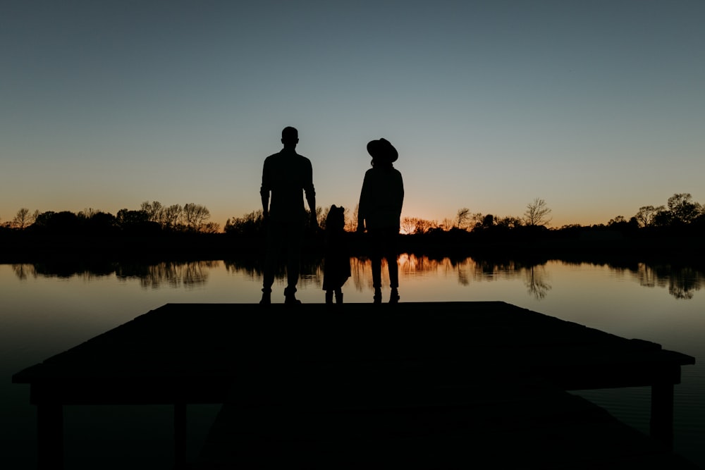 silhouette of 2 person standing on dock during sunset