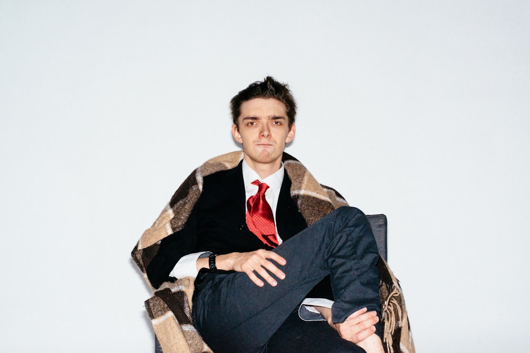 man in black suit jacket sitting on brown wooden armchair