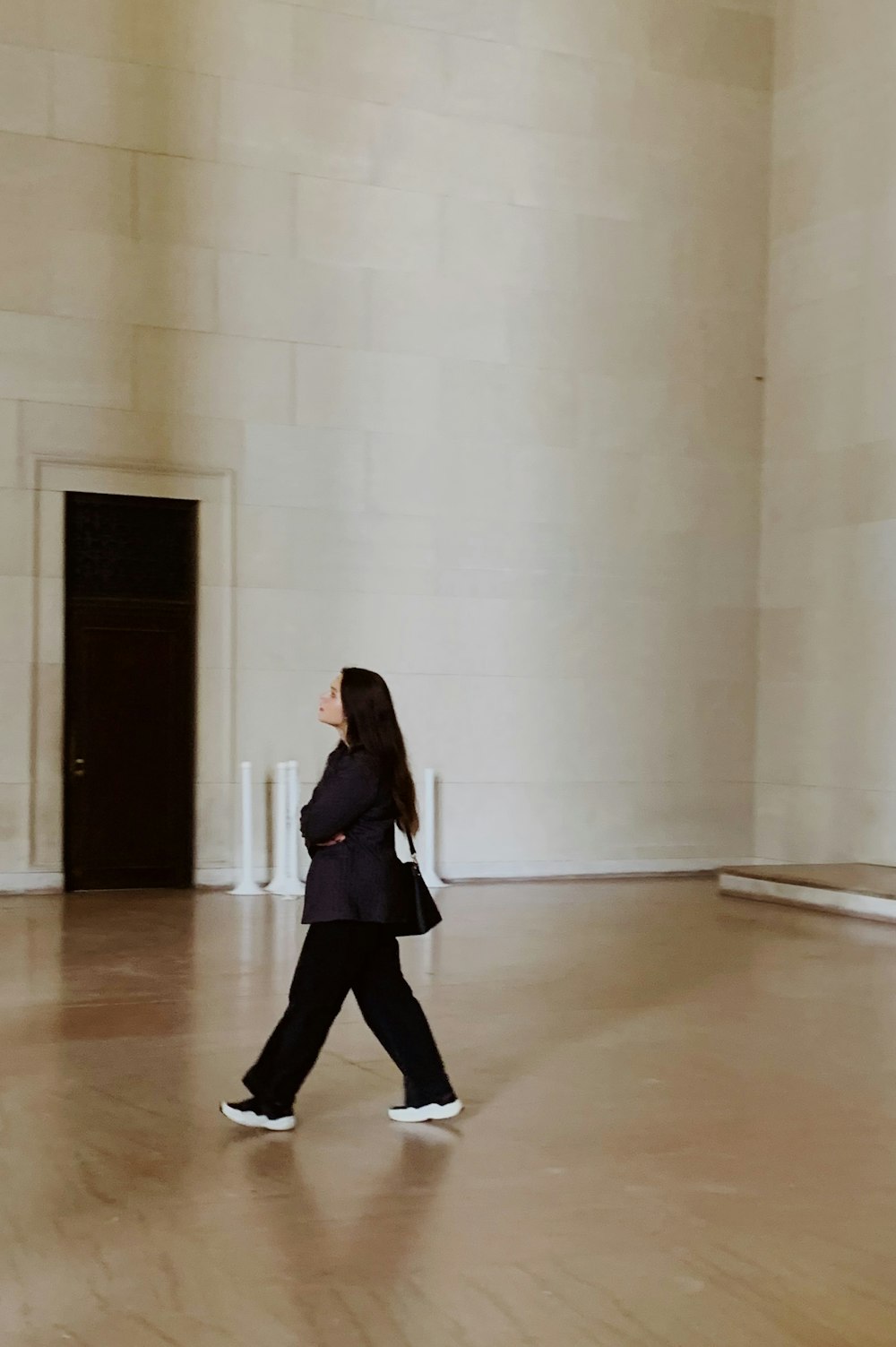 廊下に立つ黒い長袖シャツと黒いズボンの女性