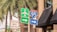 A collection of road signs located at a busy intersection, with an Interstate 95 sign, an airport directional sign, and other traffic instructions. Palm trees and a building with a Hertz sign are in the background.